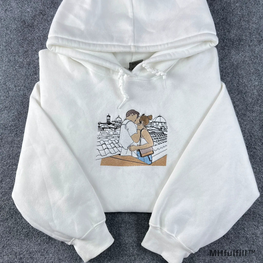 Flatlay view of a premium white custom embroidered hoodie with drawstring on a grey textured background.