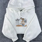 Flatlay view of a premium white custom embroidered hoodie with drawstring on a grey textured background.