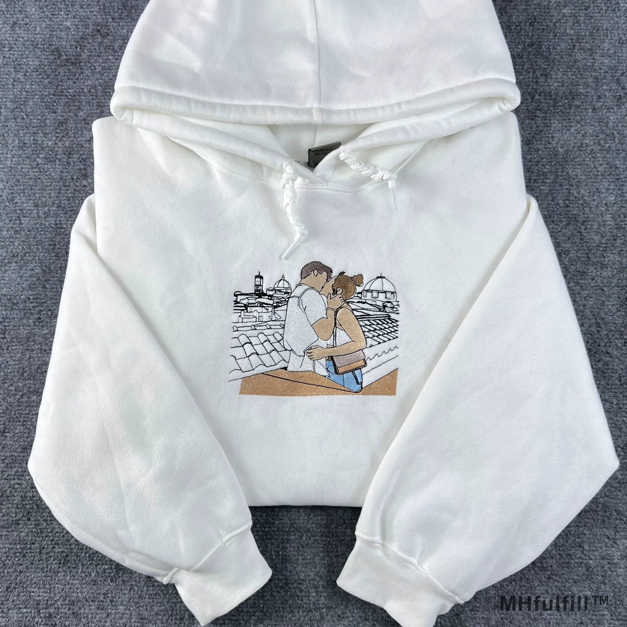 Flatlay view of a premium white custom embroidered hoodie with drawstring on a grey textured background.