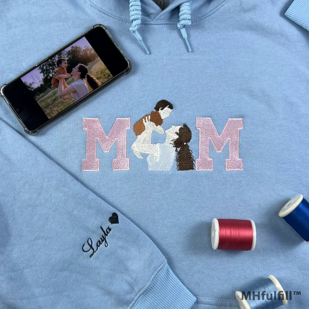 A woman holding a personalized light blue mama crewneck sweatshirt with high-quality custom thread embroidery.