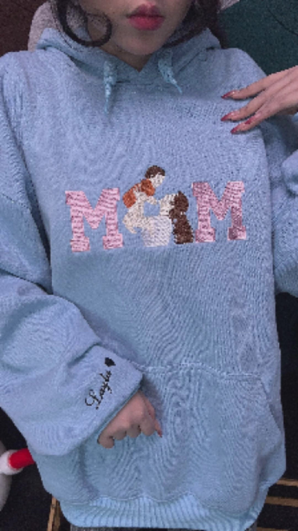A woman holding a personalized light blue mama crewneck sweatshirt with high-quality custom thread embroidery.