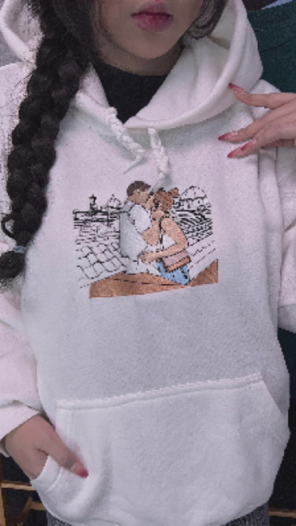 White custom line art hoodie showing an embroidered romantic couple hugging in a scenic city backdrop.