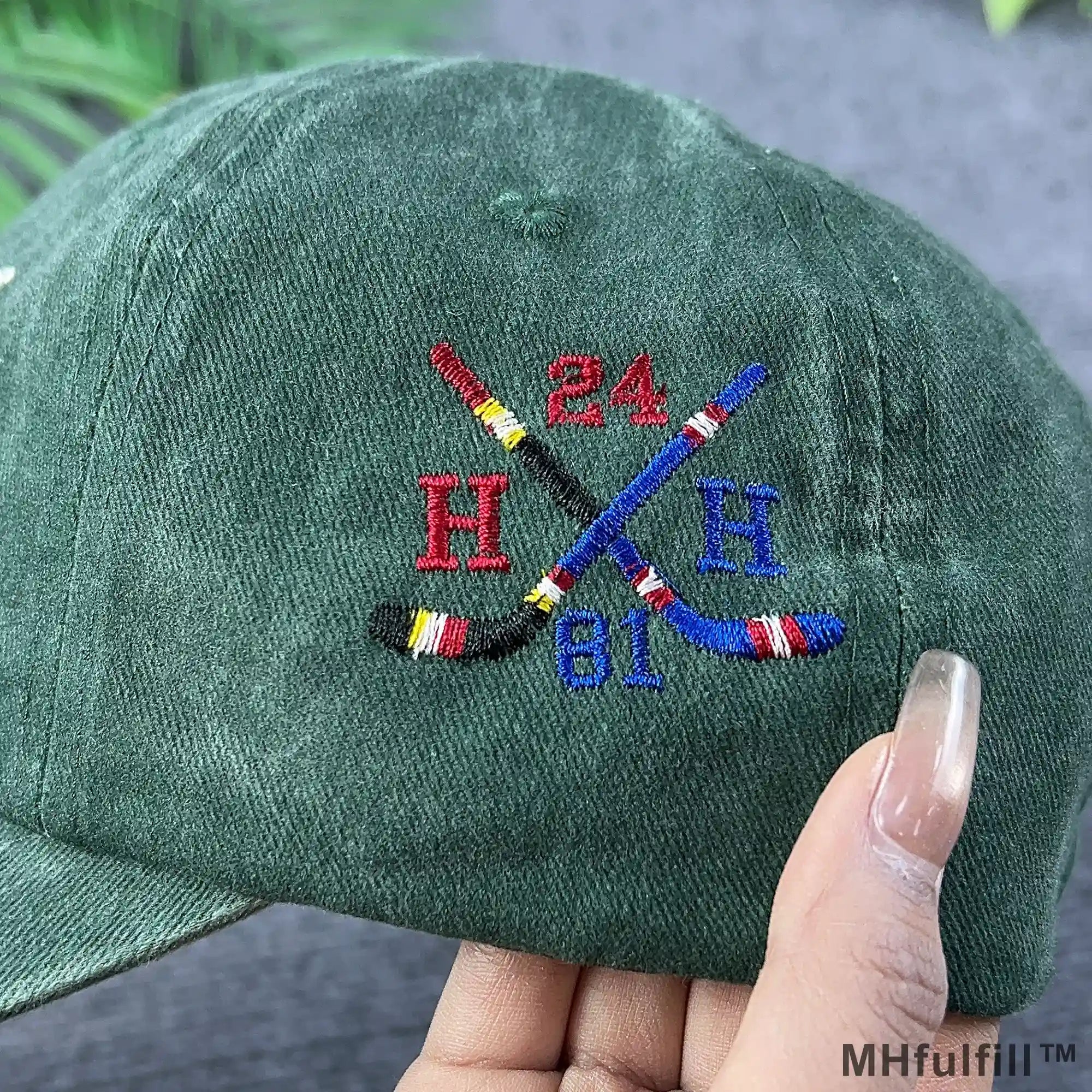 Side view of MHFulfill green baseball cap showing retro crossed hockey sticks embroidery with numbers 24 and 81.